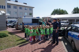 policjant stojący przy radiowozie pokazuje grupie dzieci tarczą do zatrzymywania znak stop