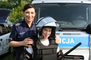 policjantka na tle radiowozu z dzieckiem ubranym w strój szturmowy policjanta