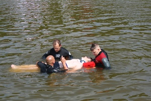 chłopak na noszach unoszących się w wodzie z ratownikami
