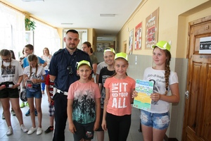 policjant z dziećmi w odblaskowych czapkach