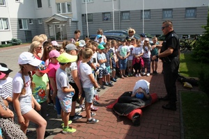 policjant prezentuje z chłopcem dzieciom bezpieczną pozycję żółwia