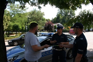 dwóch policjantów i mężczyźna stoją na chodniku. Funkcjonariusze wręczają mu opaskę odblaskową