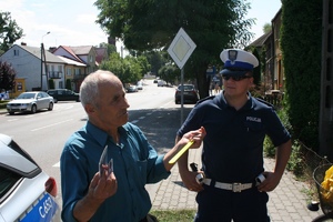 funkcjonariusz stoi na chodniku ze starszym mężczyzną, który trzyma w ręku opaskę odblaskową